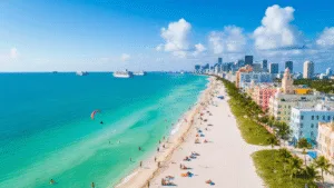"Aerial view of Miami Beach with Art Deco buildings, palm trees, colorful beach umbrellas, hotel pools, yachts, and beachgoers on a sunny day"