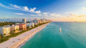 Miami in October: Your Ultimate Tropical Playground Awaits (Without the Summer Sweat) "Aerial drone shot of Miami Beach at sunset in October, featuring turquoise waters, white sandy beaches, palm trees, Art Deco buildings of South Beach, sailboats, and beachgoers in perfect weather conditions."
