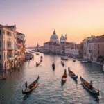 "Aerial view of Venice at sunset featuring the Grand Canal, gondolas, Rialto Bridge, St. Mark's Basilica, and Venetian Gothic architecture."