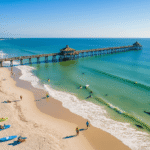 Why Cocoa Beach in February is Your Secret Winter Paradise "Aerial view of Cocoa Beach in winter featuring golden sand, surfing waves, iconic pier, kayakers in Banana River Lagoon, dolphins, manatees, beachgoers, and stretching coastline of Space Coast."