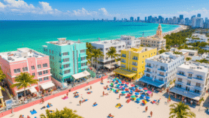 "Aerial view of a vibrant South Beach Miami in summer with pastel Art Deco buildings, bustling beach activities, colorful lifeguard towers, and the city skyline under a bright blue sky"
