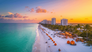 "Sarasota's coastline with Siesta Key Beach, palm trees, fall festival decors, crystal-clear turquoise waters, orange and pink sky, ROCKtoberfest and Halloween signs, modern skyline, umbrellas, and beachgoers in autumn at sunset."