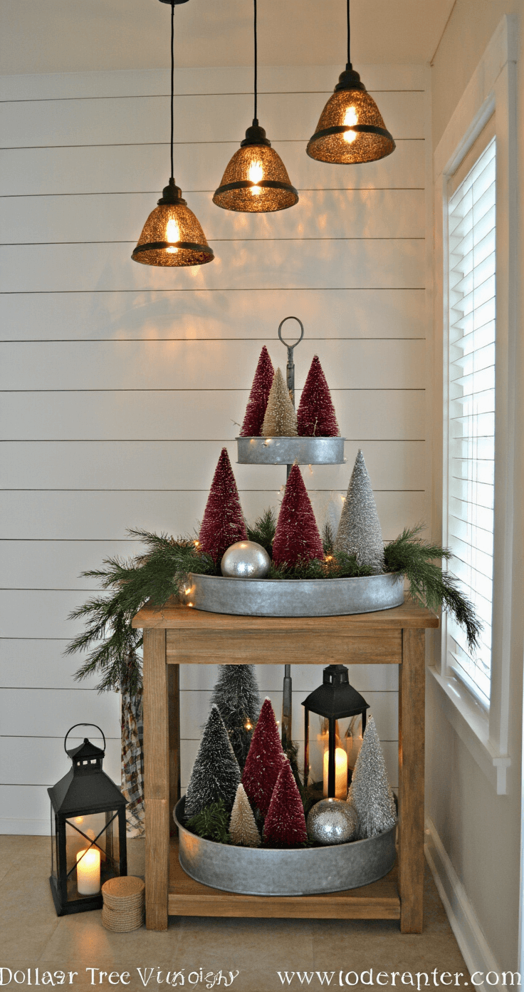 A cozy entryway vignette decorated for Christmas, featuring a rustic wooden console table with a tiered display of bottle brush trees, galvanized metal tray with burgundy and silver ornaments, vintage-style lanterns, and fresh greenery, illuminated by pendant and fairy lights against a warm white shiplap wall.