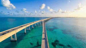The Seven Mile Bridge Drive That Changed Everything I Thought About Florida Road Trips "Panoramic view of Seven Mile Bridge in Florida, with old pedestrian walkway beside modern highway bridge, viewed over turquoise waters with visible ocean floor and distant dolphins, during golden hour"